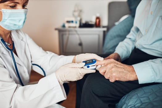 Doctor measuring the degree of oxygen saturation of the blood and heart rate of senior patient using pulse oximeter. Home treatment of virus. Checking health condition. Coronavirus pandemic. Covid-19 outbreak