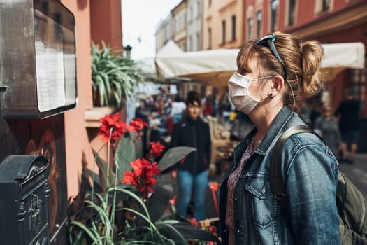 Young woman standing in a street downtown looking to the side wearing the face mask to avoid virus infection and to prevent the spread of disease in time of coronavirus