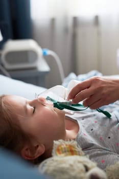 Doctor visiting little patient at home. Child having medical inhalation treatment with nebuliser. Girl with breathing mask on her face. Woman wearing uniform and face mask