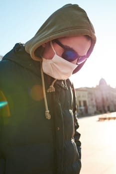 Young man in the hood wearing the face mask to avoid virus infection and to prevent the spread of disease. Walking in city centre. Virus infection protection. Real people, authentic situations