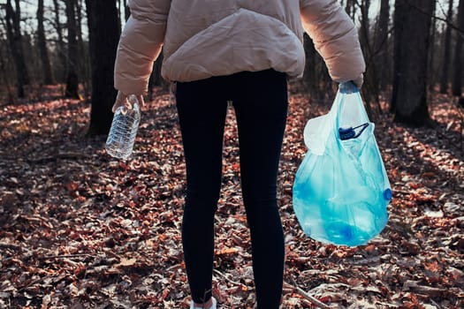 Young woman cleaning up a forest. Volunteer picking plastic waste to bags. Concept of plastic pollution and too many plastic waste. Environmental issue. Environmental damage. Responsibilitiy for environment. Real people, authentic situations