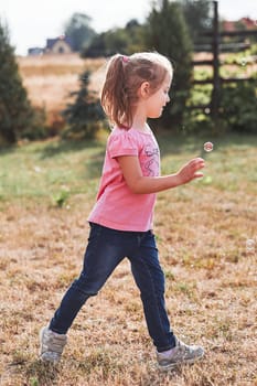 Little girl playing with soap bubbles outdoors on summer day. Real people, authentic situations