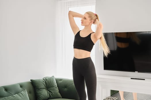 Active blonde woman does twisting exercises in bright apartment