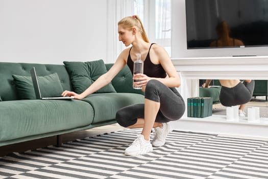 Young active woman does training exercises at home and follows an online course video on laptop