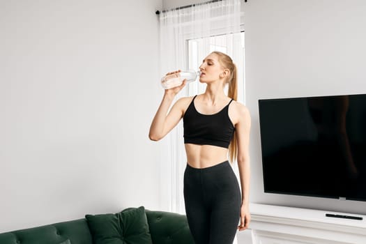 Young active woman drinks water during sport activity at home