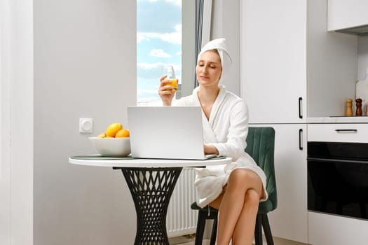Young woman wearing bathrobe checking mail while having breakfast