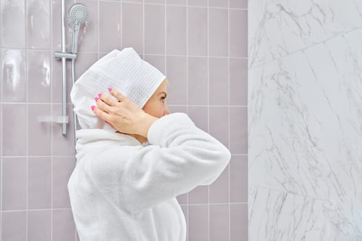 Middle aged woman in bathrobe wrapping her hair in towel after shower