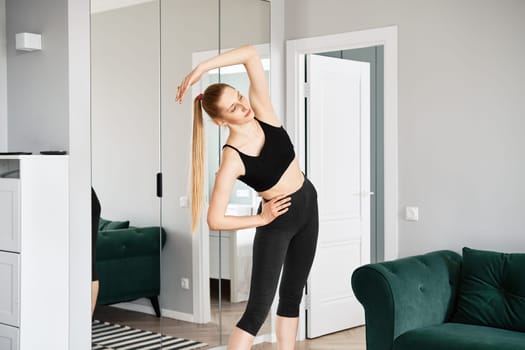 Active blonde woman does bending exercises in bright apartment