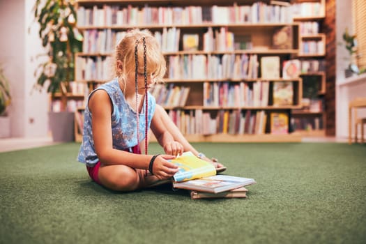 Schoolgirl reading and watching book in school library. Doing homework. Books on shelves in bookstore. Learning from books. Back to school. Elementary education