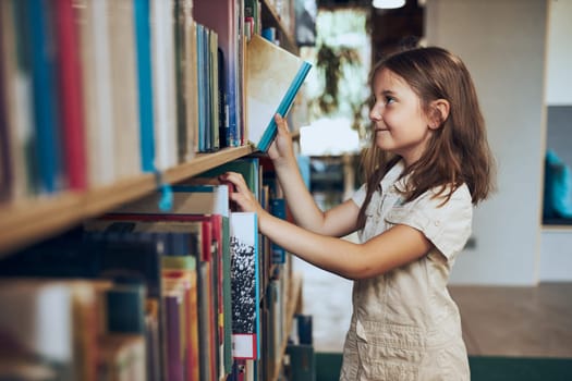 Schoolgirl choosing book in school library. Smart girl selecting literature for reading. Books on shelves in bookstore. Learning from books. School education. Benefits of everyday reading. Child curiosity. Back to school
