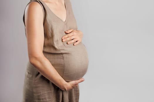 Pregnant woman touching her tummy standing over plain background. Pregnancy, expectation, motherhood concept