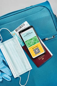 Digital covid certificate. Vaccination digital pass. Digital medical pass, passport, airplane ticket and face mask on travel bag. Digital covid vaccination pass on mobile as medical pass for travel during covid-19 pandemic. Preparing for travel
