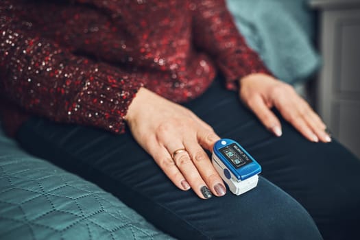 Woman measuring the degree of oxygen saturation of the blood and heart rate at home using pulse oximeter. Home treatment of virus. Checking health condition. Coronavirus pandemic. Covid-19 outbreak