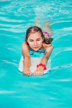 Woman learning to swim, practicing in swimming pool using a board. Candid people, real moments, authentic situations