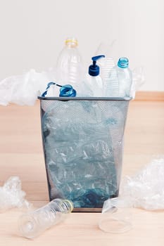 Heap of plastic bottles, cups, bags collected to recycling and scattered around a metal bin. Concept of plastic pollution and too many plastic waste. Trash with used plastic packagings over grey background with copy space at the top