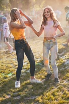 Portrait of happy smiling young girls with colorful paints on faces and clothes. Two friends spending time on holi color festival