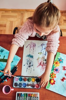 Little girl preschooler painting a picture using colorful paints and crayons. Child having fun making a picture during an art class in the classroom