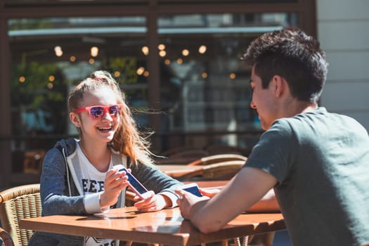 Young woman and man sitting in pavement cafe a the table talking and using mobile phones