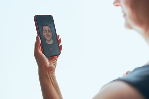 Woman having video call on mobile phone. Mature woman remotely working from office holding smartphone at front of window. Female manager using digital device. Remote communication. Video calling. Remote work