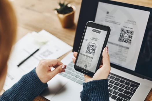 Woman scanning QR code from invoice to make payment using fast secure payment system and smartphone code reader. Business woman paying bills using express payment technology. Female using mobile phone and laptop. Paying expenses online. QR scanner. Making payment