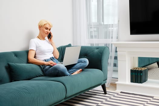 Middle-aged woman solves everyday problems remotely using laptop and smartphone