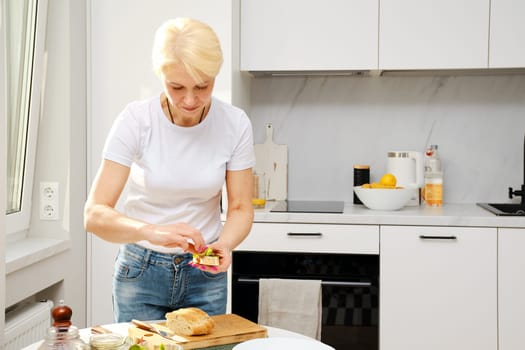 Middle aged woman puts fresh arugula and swiss chard leaves on sandwich