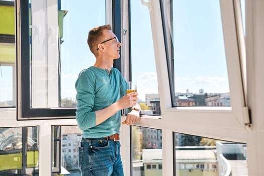 Middle aged man in glasses stands on balcony of high-rise building