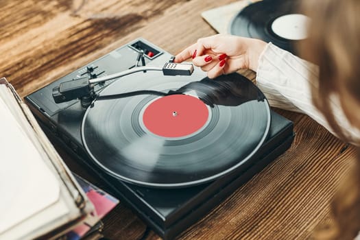 Young woman listening to music from vinyl record player. Playing music on turntable player. Female enjoying music from old record collection at home. Stack of analog vinyl records. Retro and vintage music style. Music Passion and hobby
