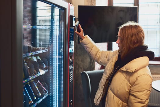 Woman paying for product at vending machine using contactless method of payment with mobile phone. Woman using new way of payments