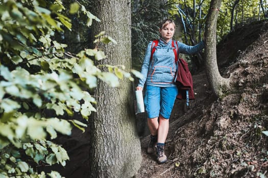 Active woman walking on forest path, actively spending summer vacation, carrying backpack, holding map