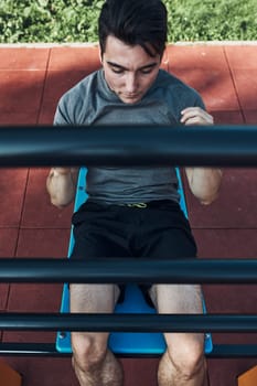 Young man doing sit-ups during his workout in a modern calisthenics street workout park. Man sitting on a sit-up board wearing sportswear