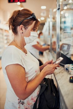 Woman shopping at pharmacy, buying medicines, wearing face mask to cover mouth and nose during pandemic coronavirus outbreak