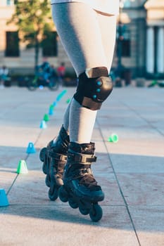 Young girl training the riding on roller skates. Closeup of female legs with roller skates and protectors