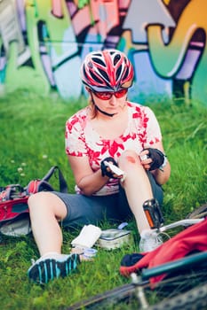 Woman dressing the wound on her knee with medicine in spray and gauze on bike trip on summer day