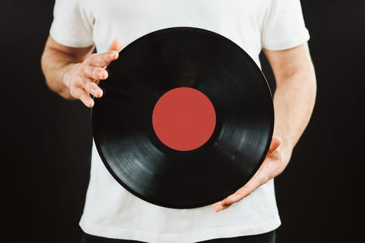 Man with vinyl record. Vintage music style. Male holding black analog disk standing on black background. Retro music. Classic audio