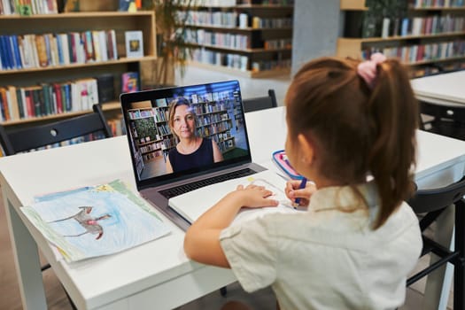 Student litttle girl having video class remotely with her teacher on laptop sitting at desk in after school club at primary school. Back to school. Child using technology on elementary computer science lesson. Smart little girl learning online. Teacher teaching remotely. E-learning classes