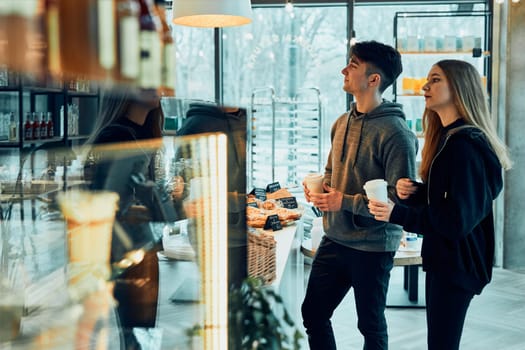 Friends doing shopping in a coffee shop. Young man and woman having chat while picking out the pastry, bakery's goods and hot drinks standing at counter in a coffee shop. People buying coffee and sweet snacks to go