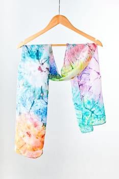Silk colourful hand painted tied scarf hung on hanger over grey background. Woman fashion, tying a scarf, wearing a scarves. Stylish ways to tie and wear scarves
