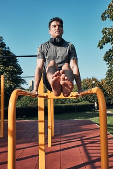 Young man doing L-Sit on parallel bars during his workout in a modern calisthenics street workout park. Man wearing sportswear looking away