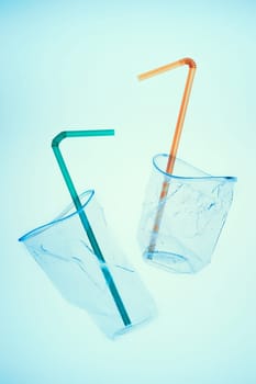 Squashed plastic cups and drink straws over blue background. Collecting plastic waste to recycling. Concept of plastic pollution and too many plastic waste. Copy space at the top