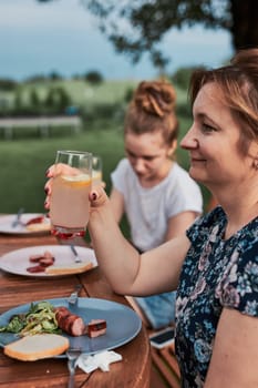 Family having a meal from grill during summer picnic outdoor dinner in a home garden. Close up of people sitting at a table with food and dishes