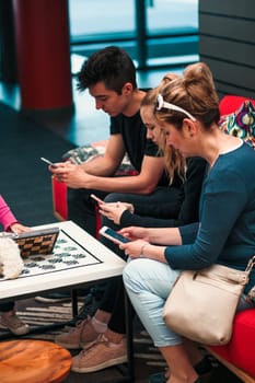 Family members using mobile phones together, sitting on sofa in lounge in hotel