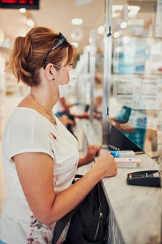 Woman shopping at pharmacy, buying medicines, wearing face mask to cover mouth and nose during pandemic coronavirus outbreak