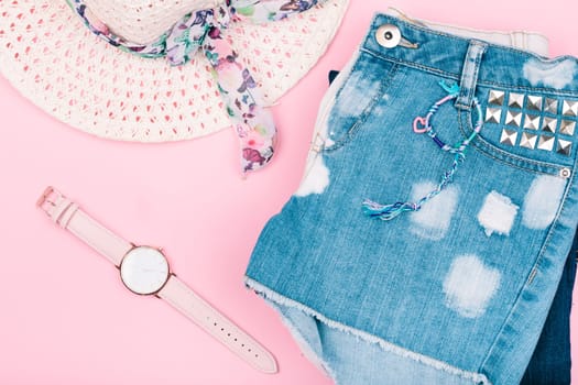 Female girlish clothes, blue jeans shorts, hat, watch on pink background
