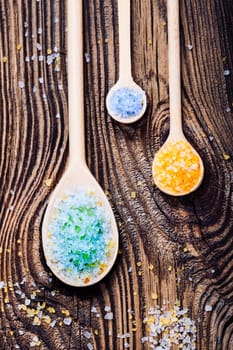 Colorful sea salt in wooden spoons put on old wooden table. Photo from above