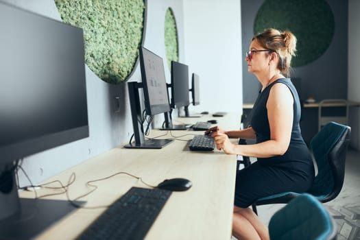 Concerned businesswoman working on computer in office. Busy woman sitting at desk at front of computer monitor. Focusing on work. Open office. Copy space left