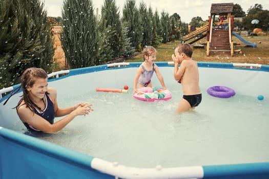 Children splashing, jumping, playing in a pool in backyard on summer vacation day. Real people, authentic situations
