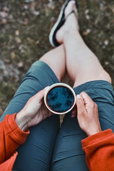 Close up of woman sitting outdoors holding cup with coffee. Reflection of trees in a coffee. View from above