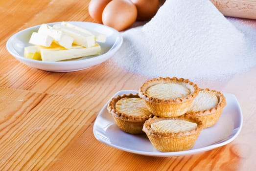 Freshly made apple pies on the table with flour eggs and butter