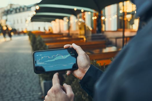 Person investing trading on stock cryptocurrency market using investing application on smartphone. Stock market investment in hand. Trader holding mobile phone looking at candle chart